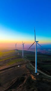 Aerial view of wind turbines on green hills during a vibrant sunset, showcasing renewable energy.