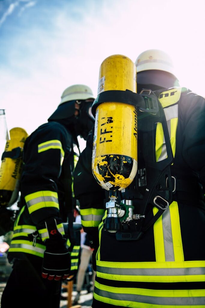 Firefighters wearing safety gear and oxygen tanks during a daytime emergency scene.