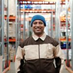 Happy warehouse worker smiling in a storeroom wearing a blue beanie and uniform.