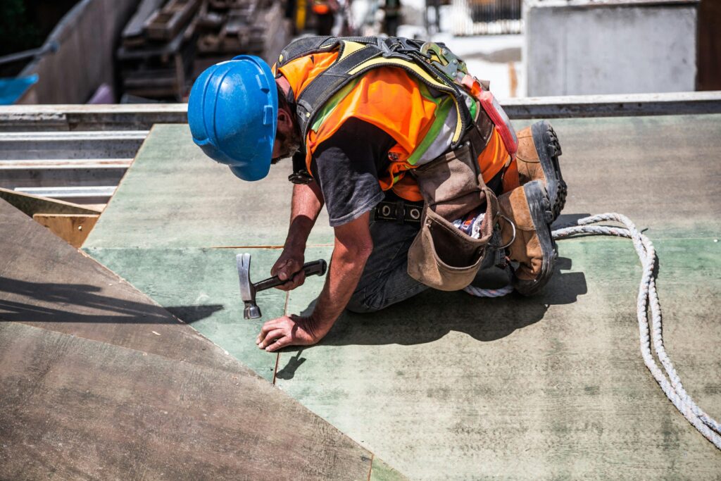 A skilled construction worker in protective gear hammering a rooftop panel.