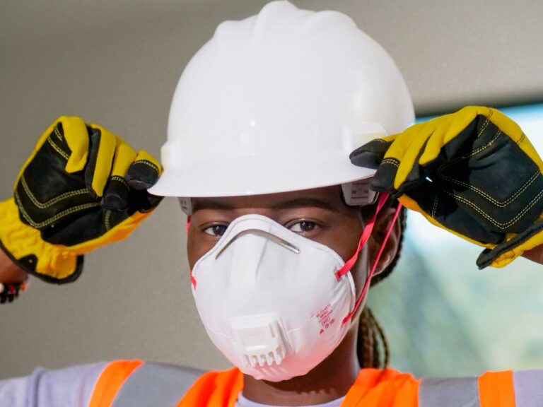 Construction worker wearing hardhat, N95 mask, and gloves for safety.